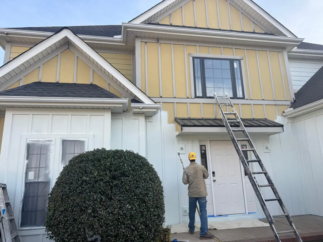 Painter rolling white paint over yellow siding on a house in Greenville, SC